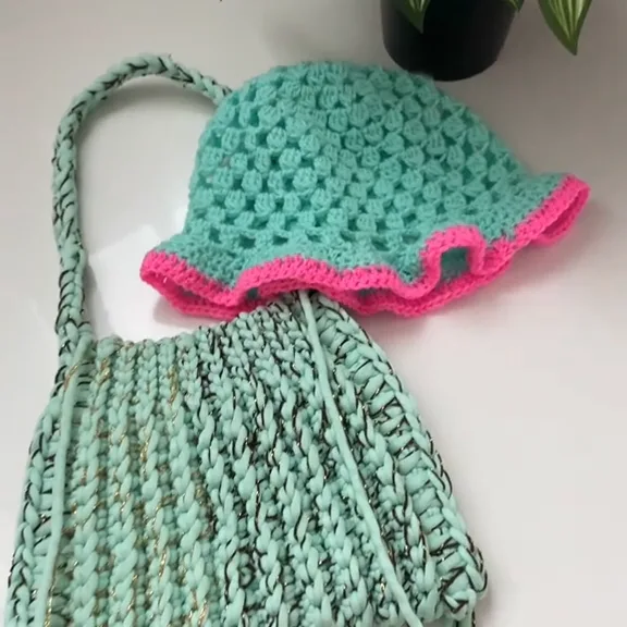 Turquoise crochet bucket hat with a wavy neon pink brim, resting on a mint green crochet bag