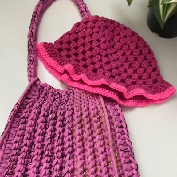 Raspberry crochet bucket hat with a wavy neon pink brim, resting on a fuchsia pink crochet bag