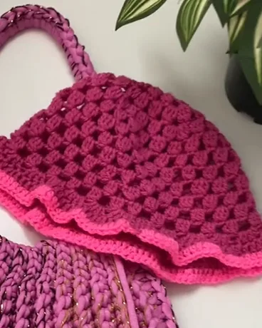 Close-up of the raspberry bucket hat: openwork crochet squares and neon pink brim