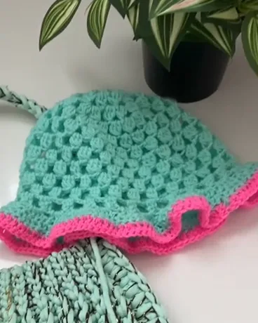 Close-up of the turquoise bucket hat: openwork crochet squares and neon pink brim