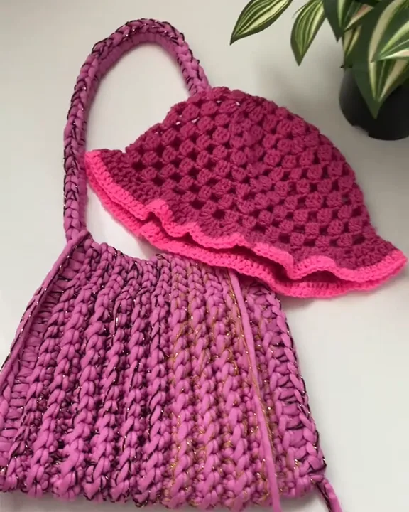 Raspberry crochet bucket hat with a wavy neon pink brim, resting on a fuchsia pink crochet bag